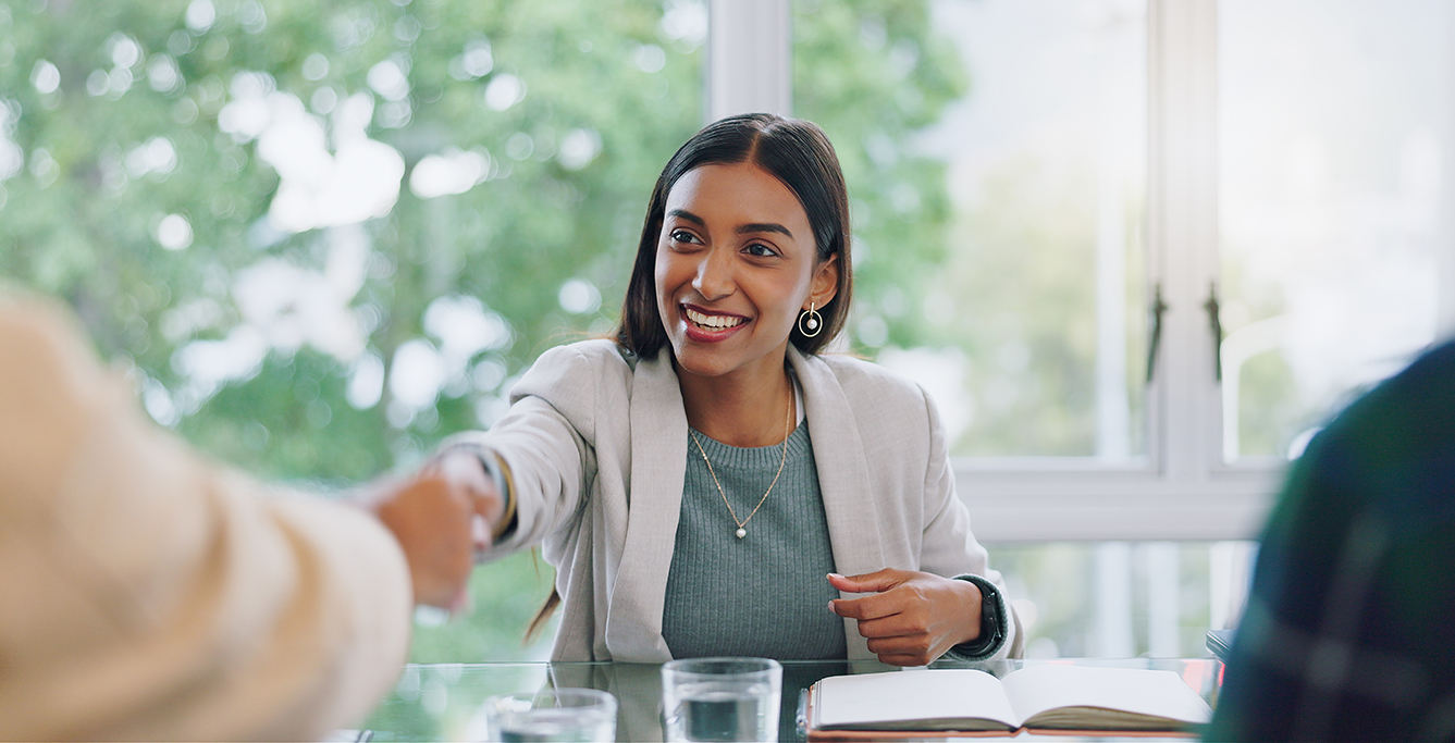 Woman in green shaking hands across a desk