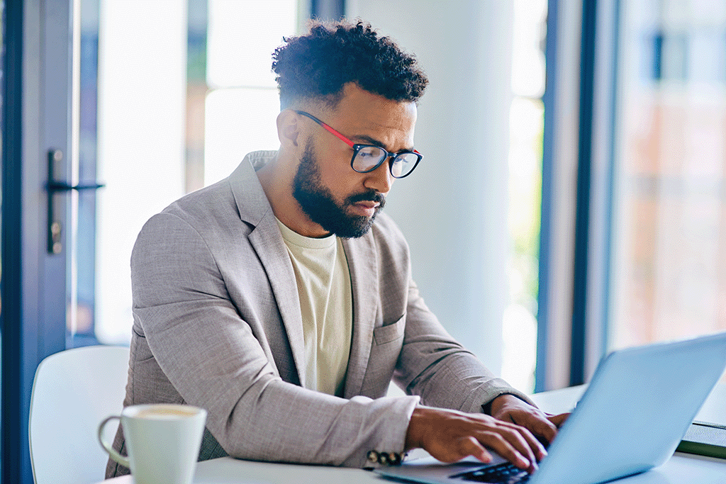 Man sitting at computer wearing glasses and drinking coffee